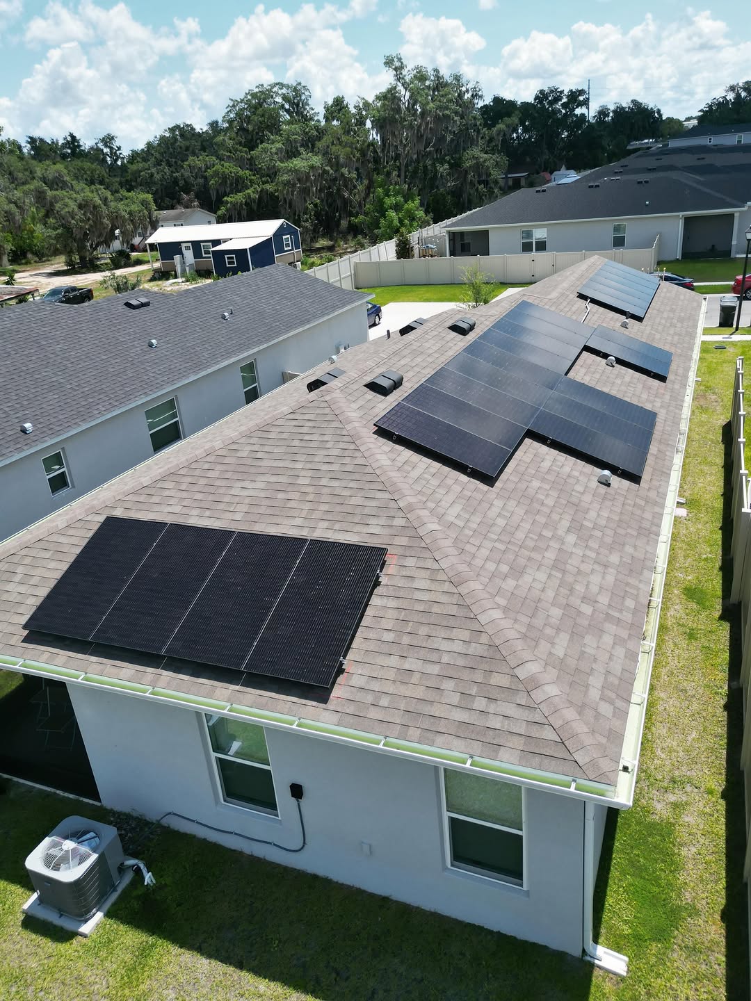 Aerial view of solar panels distributed across a shingle roof on a single-story home