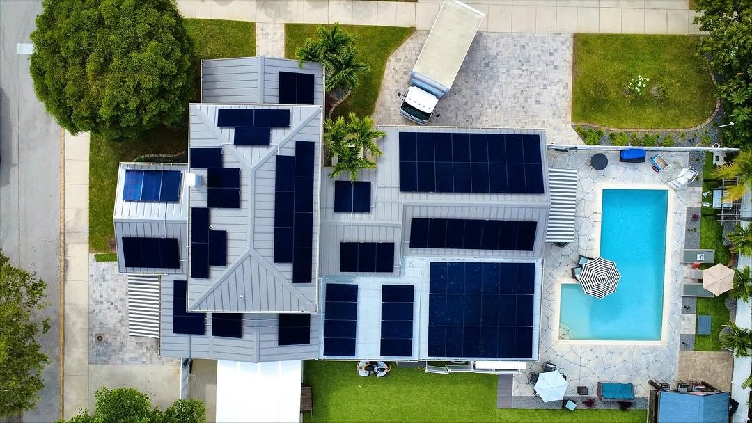 Overhead view of several solar arrays on a light metal roof beside a pool